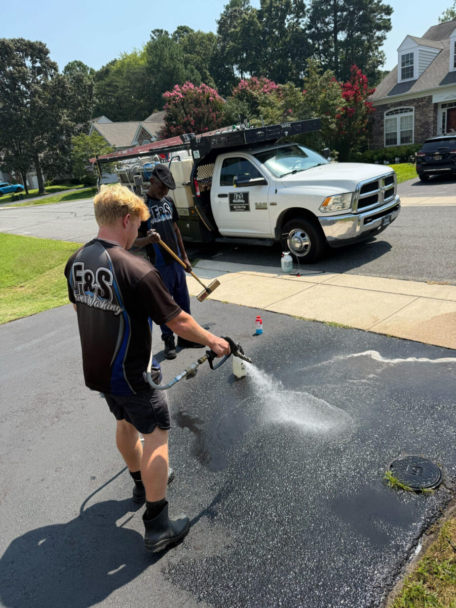 Two workers pressure washing a driveway in a residential neighborhood.